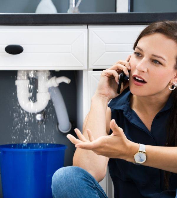woman on phone in front of leaking pipe