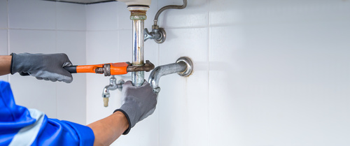 Technician plumber using a wrench to repair a water pipe under the sink. Concept of maintenance, fix water plumbing leaks, replace the kitchen sink drain, cleaning clogged pipes